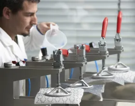 Une personne en blouse blanche versant l’eau d’un gobelet sur différents tissus, chacun fixé à un dispositif.