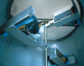 Trois chaussures tournent autour d’une tige métallique à l’intérieur d’un dispositif avec couvercle en maille métallique.