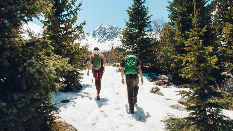 a man and a woman hiking up a snowy mountain on a sunny day