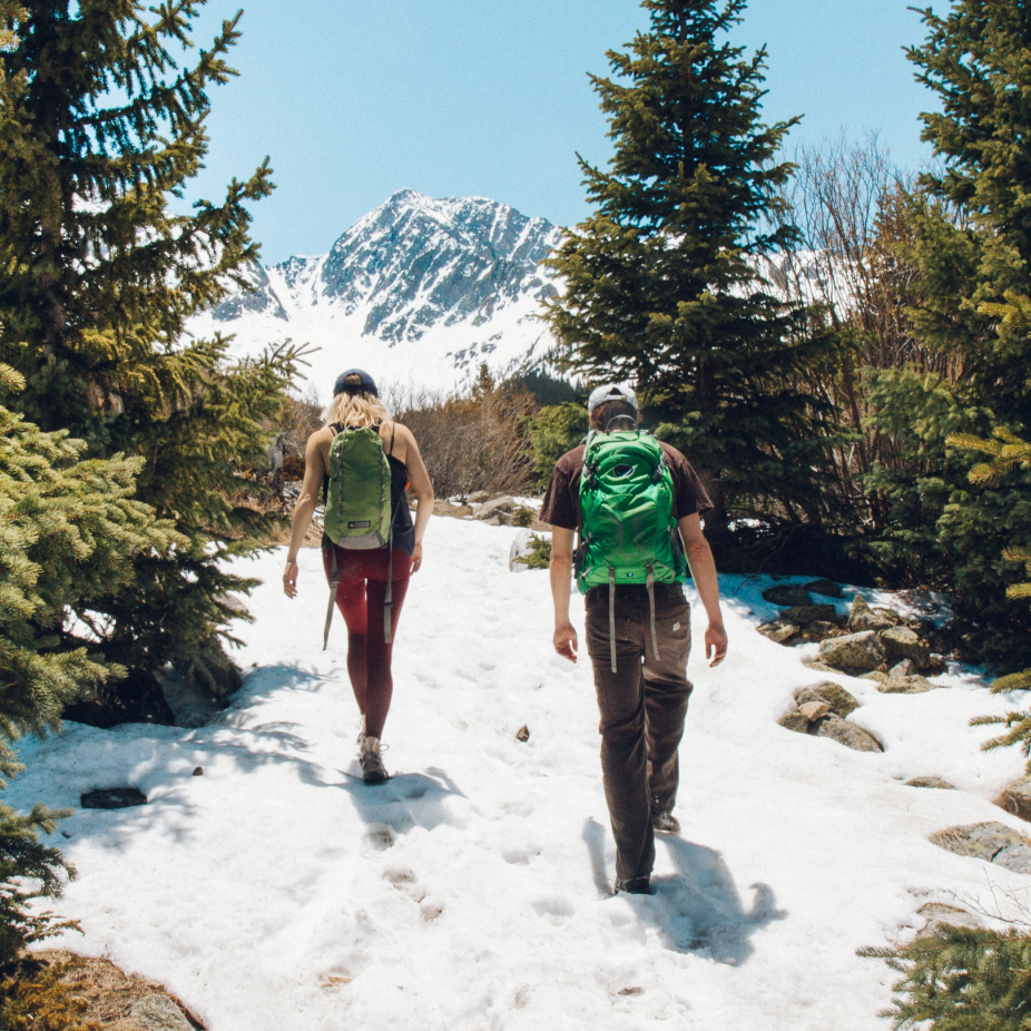 a man and a woman hiking up a snowy mountain on a sunny day