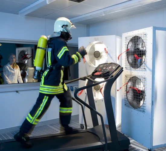 Persona vestida con un traje de bomberos caminando sobre la cinta de correr en un laboratorio de Gore.